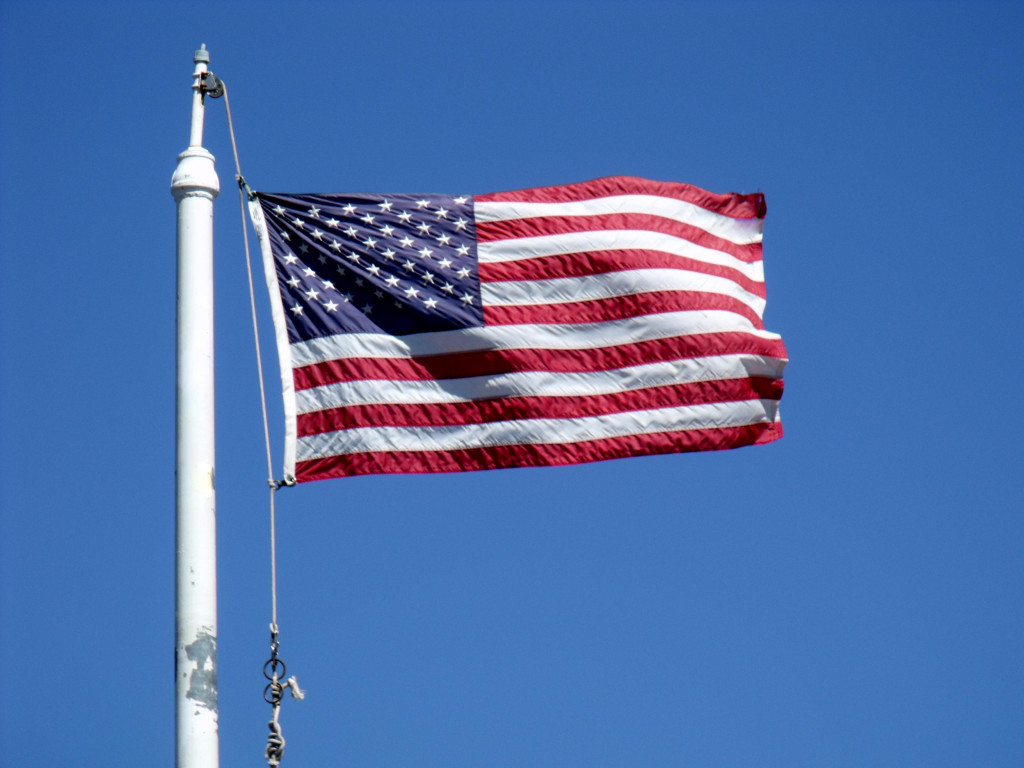 American flag waving on a pole against a clear blue sky. The stars and stripes are prominently displayed, conveying a sense of national pride and freedom.