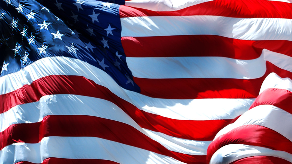 Close-up of a waving American flag. The fabric shows vibrant red and white stripes, along with blue field and white stars, conveying patriotism and pride.